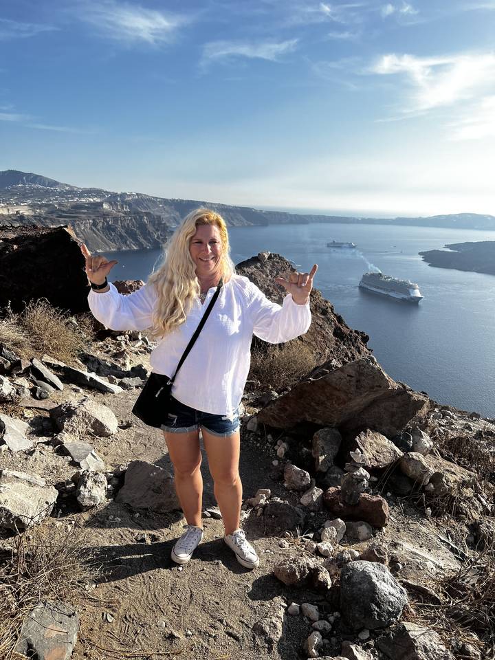 Personne qui pose sur une falaise rocheuse avec vue sur la mer et des bateaux.