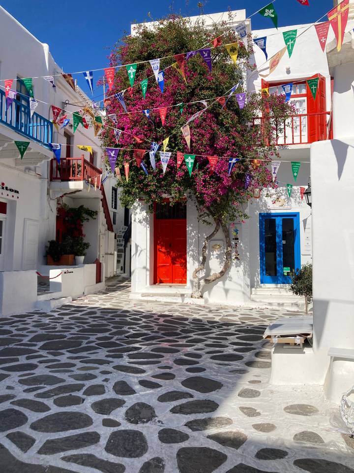 Rue colorée à Mykonos avec des fleurs et des drapeaux.