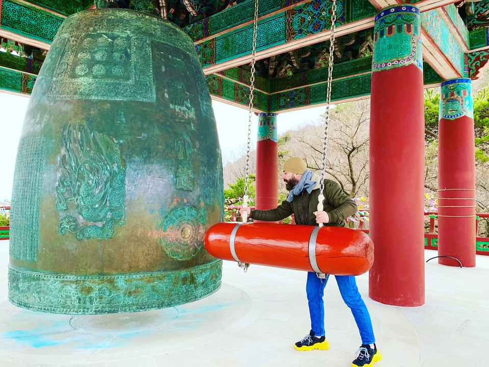 Une personne faisant sonner une grande cloche traditionnelle dans un temple aux piliers rouges.