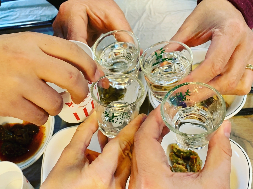 Plusieurs mains levant de petits verres remplis de liquide transparent dans une célébration.