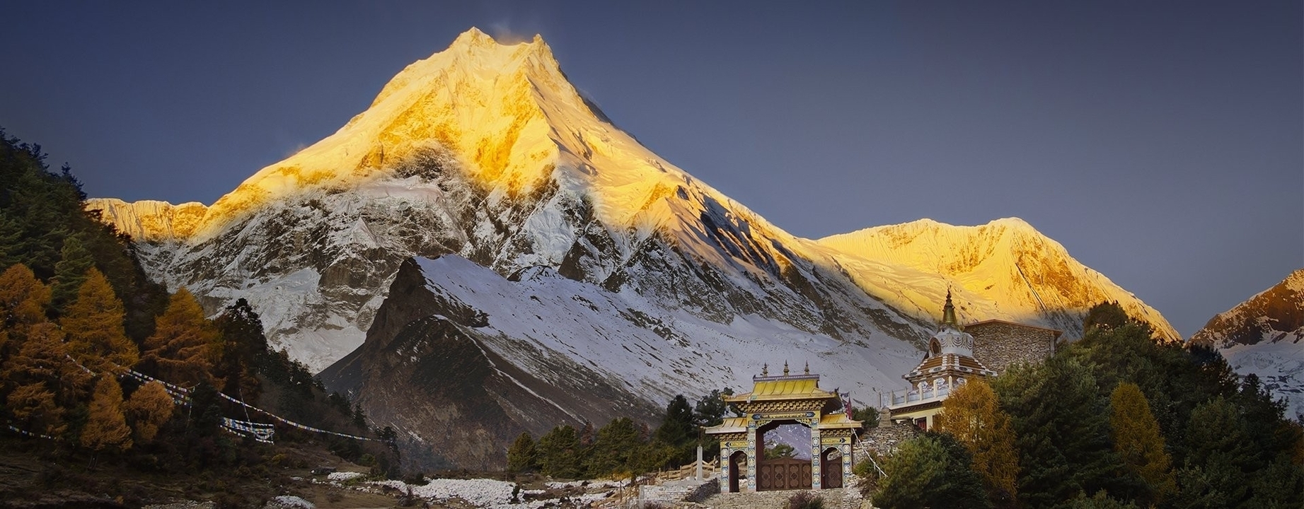 La lumière dorée du soleil illuminant une montagne enneigée avec un sanctuaire au premier plan.