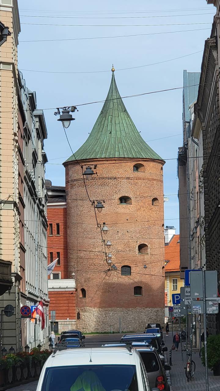 A historic round tower with a green conical roof seen from a cobbled street.