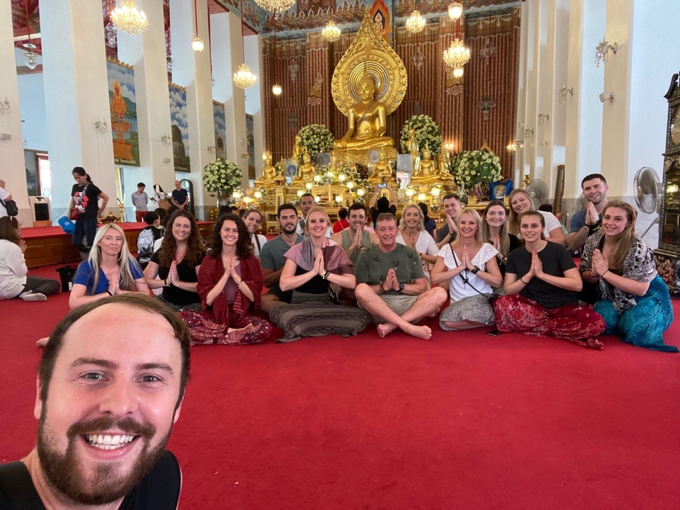 Groupe assis devant un Bouddha doré dans un temple.