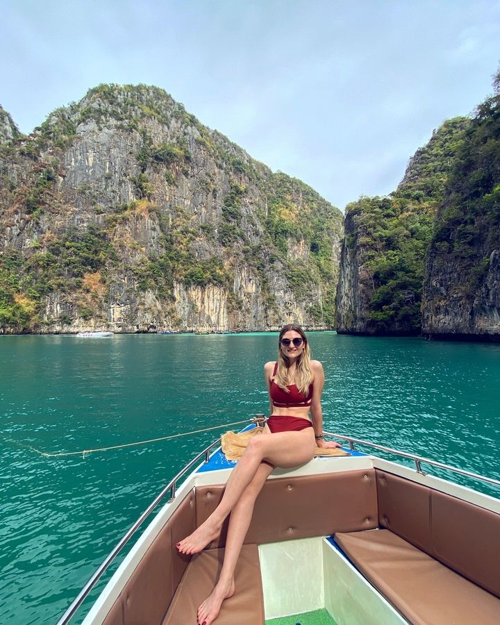 Person posing on a boat with turquoise water and cliffs.