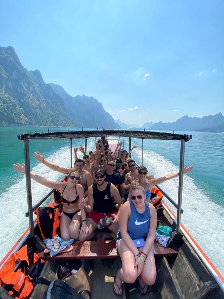 Group of people on a boat in a turquoise lake with mountains in the background.