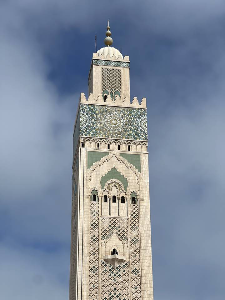 Un grand minaret aux motifs de mosaïque complexes se dressant contre un ciel nuageux.