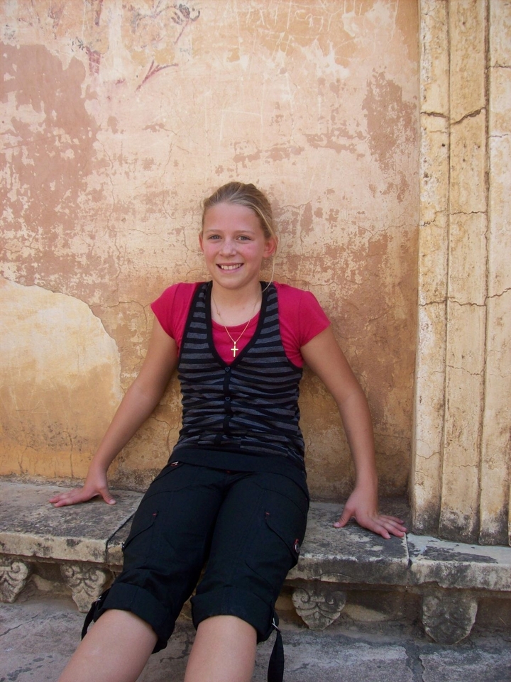 Jeune fille assise contre un mur texturé.