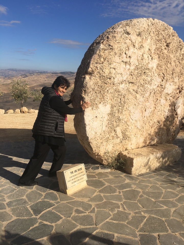 Personne posant avec un gros rocher dans un paysage désertique.