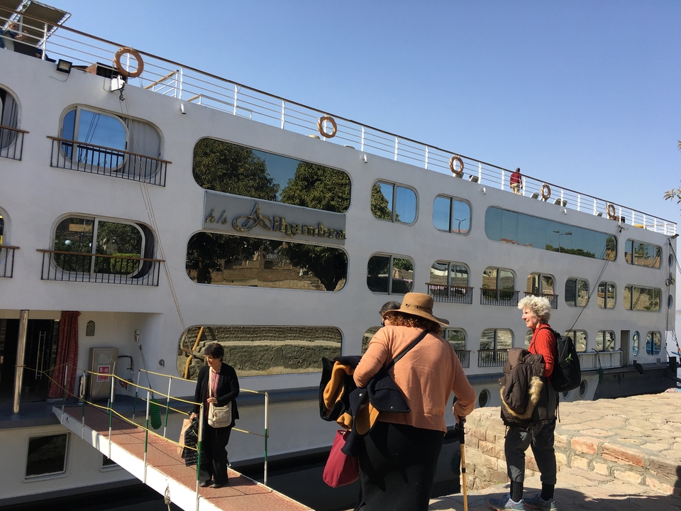 Des gens marchant à côté d'un bateau de croisière amarré sur le Nil.