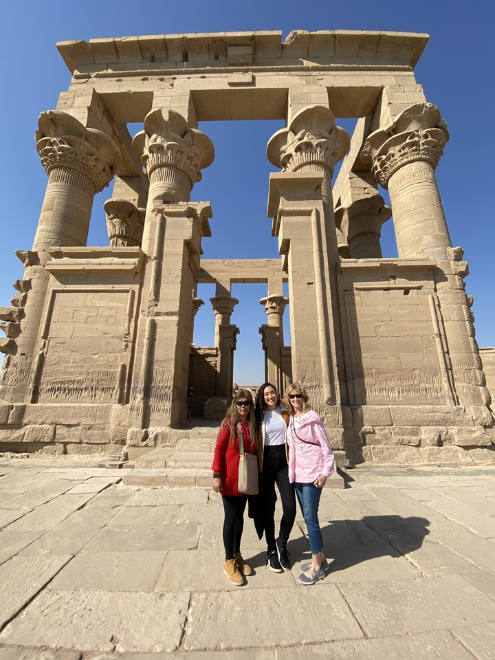 Trois femmes posant devant une structure de pierre ancienne.