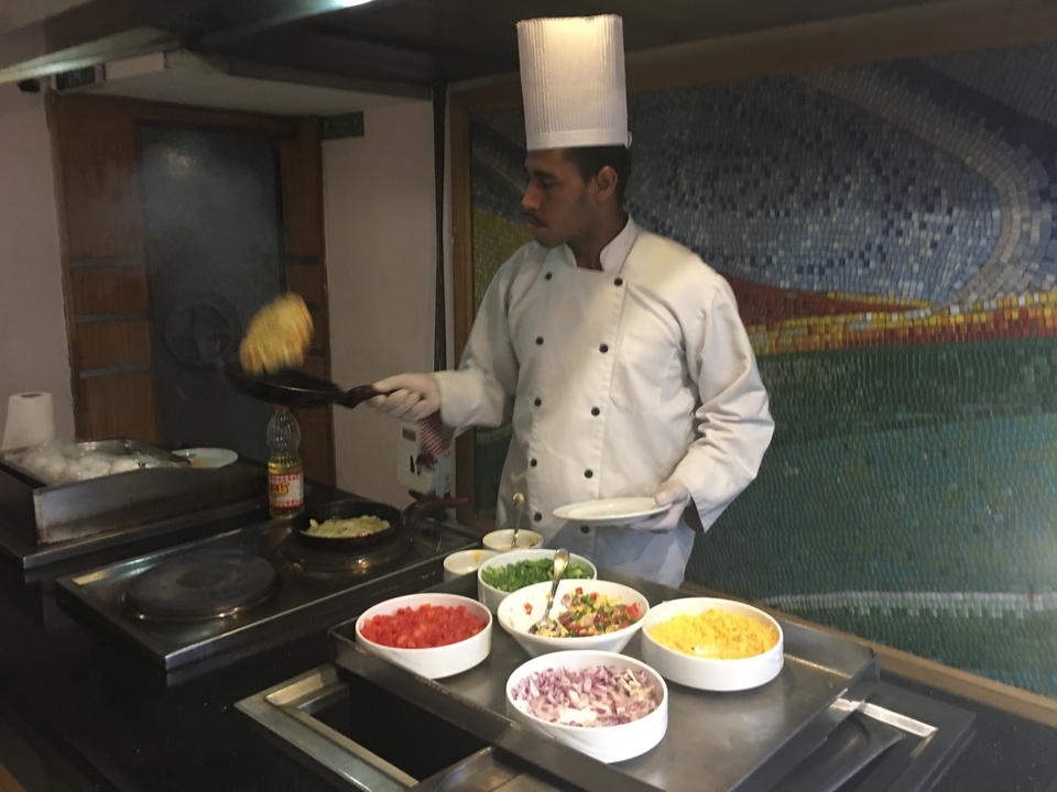 Chef préparant une omelette avec divers ingrédients à un buffet.
