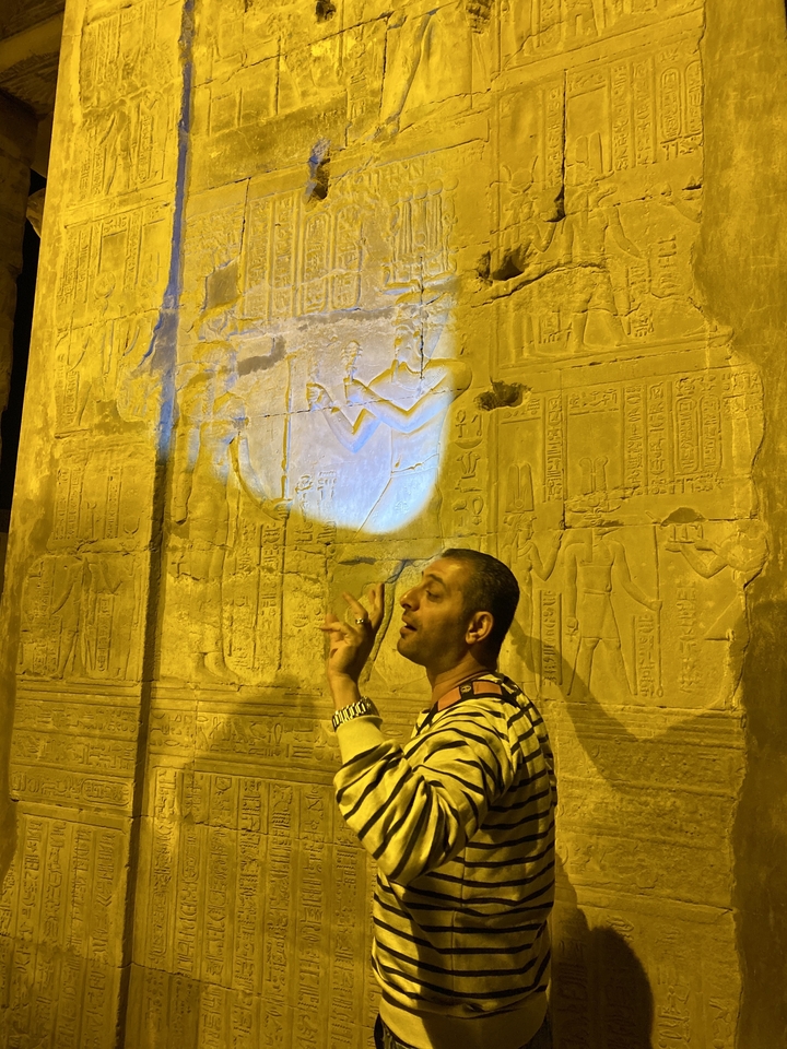 Personne gesticulant devant des sculptures égyptiennes antiques sous un éclairage artificiel.