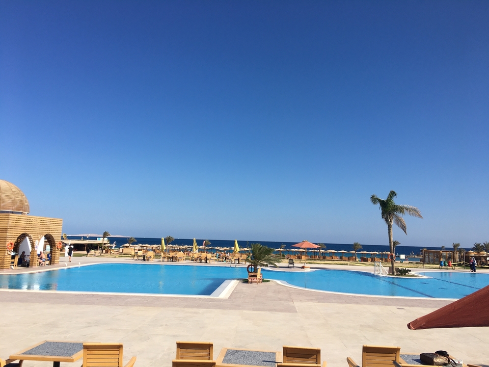 Piscine de station balnéaire avec palmiers et mer en arrière-plan.