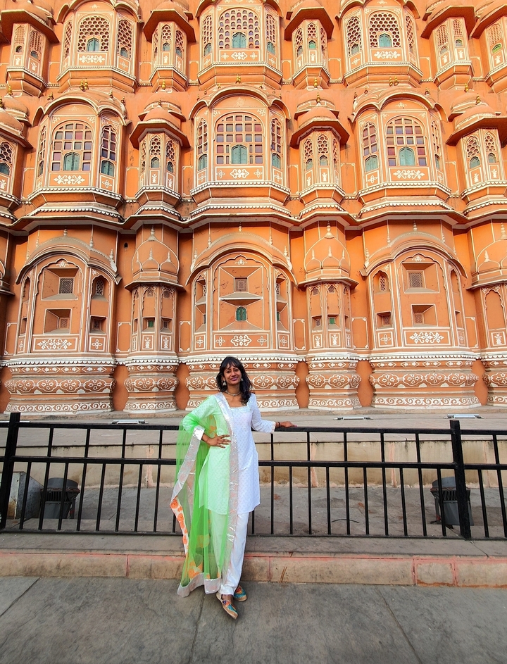 Femme posant devant la façade d'un bâtiment richement décorée.