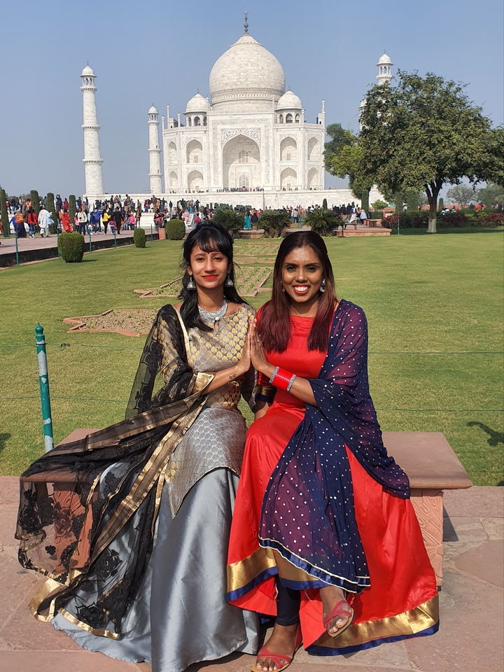 Deux femmes assises sur une pelouse avec le Taj Mahal au loin.