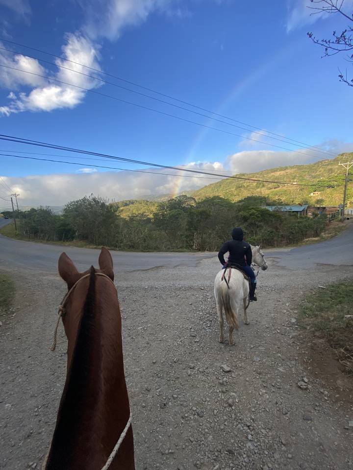 Des gens à cheval sur un chemin de terre avec un arc-en-ciel au loin.