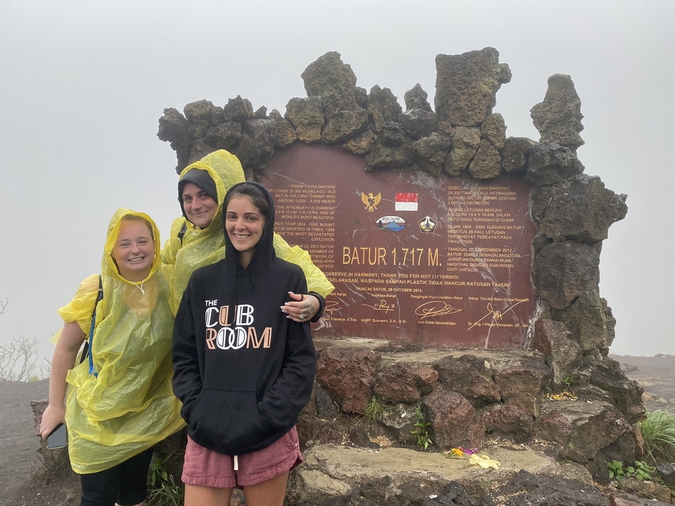 Trois personnes debout au sommet d'une montagne avec un panneau indiquant l'altitude et les coordonnées.