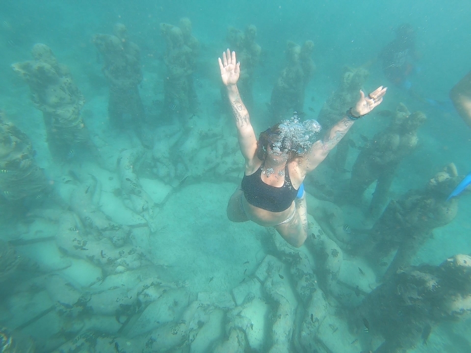 Une femme nageant joyeusement sous l'eau avec des sculptures immergées.