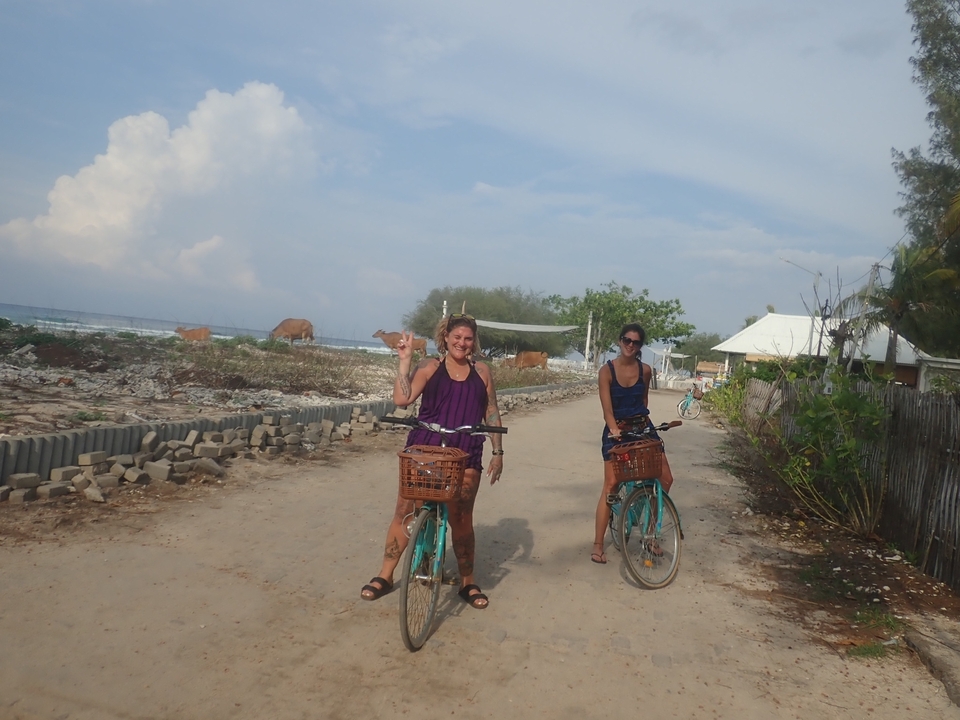 Deux femmes à vélo sur un sentier de terre avec vue sur la plage.