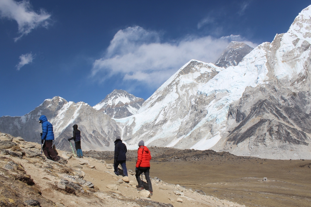 Des randonneurs marchant le long d'un sentier de montagne avec des sommets enneigés.