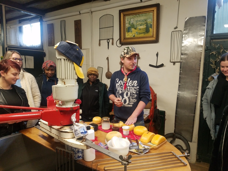 Une personne faisant une démonstration de fromage devant un groupe qui observe dans un marché.