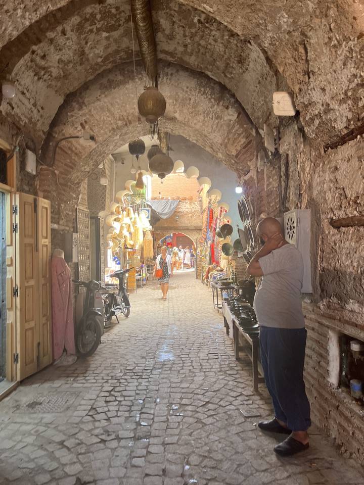 Des gens qui marchent dans un marché sous des arches de pierre.