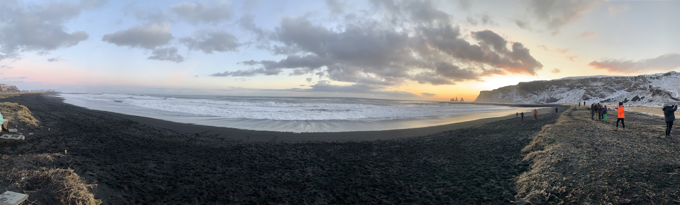 Vue large d'une plage de sable noir avec des vagues.