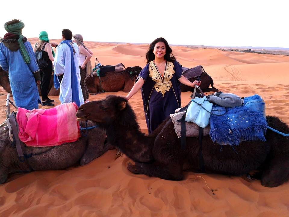 Person posing with camels in the desert.