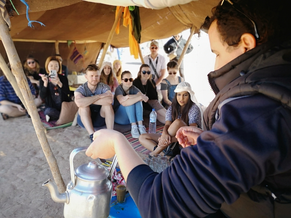 Group of people sitting under a tent having tea.