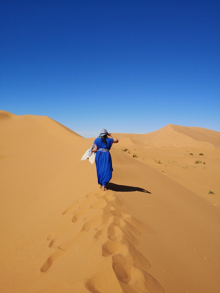 Person in blue dress walking in the desert.