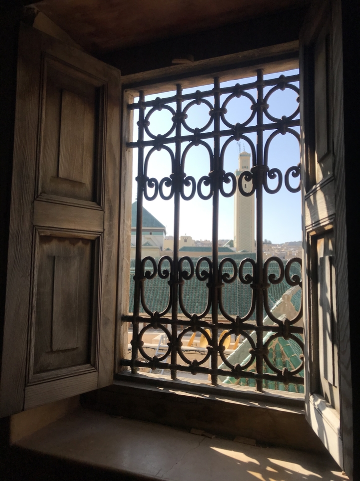 Vue à travers une fenêtre ornée avec un paysage urbain en arrière-plan.