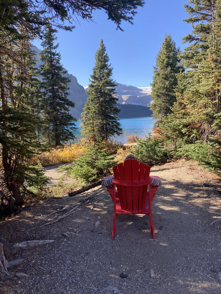 Personne assise dans un fauteuil rouge face à une vue sur un lac, entourée d'arbres.