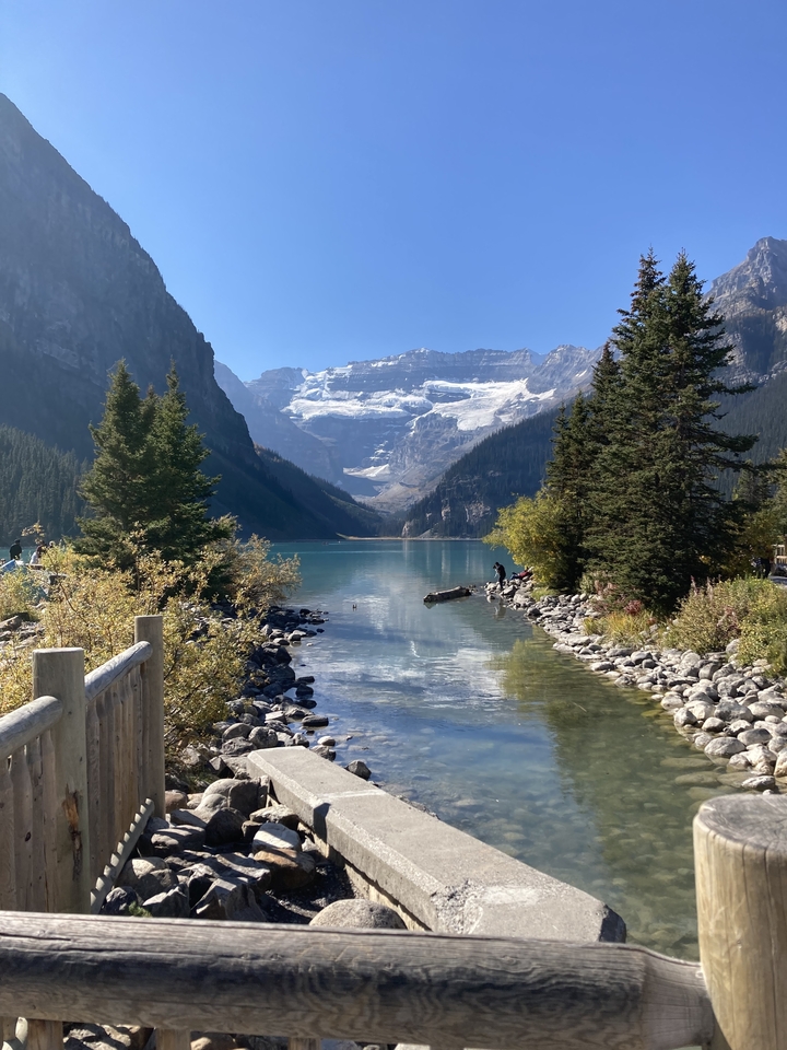 Vue panoramique d'un lac avec des montagnes et une personne debout au bord de l'eau.