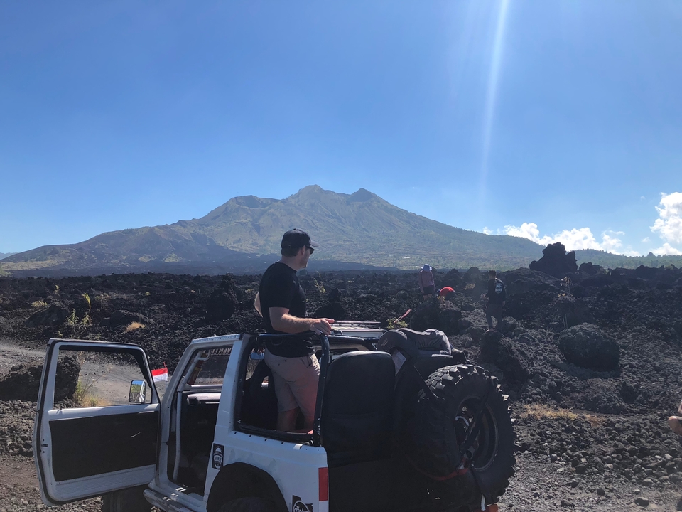 Personne debout sur une jeep blanche avec une vue sur les montagnes et les roches volcaniques.
