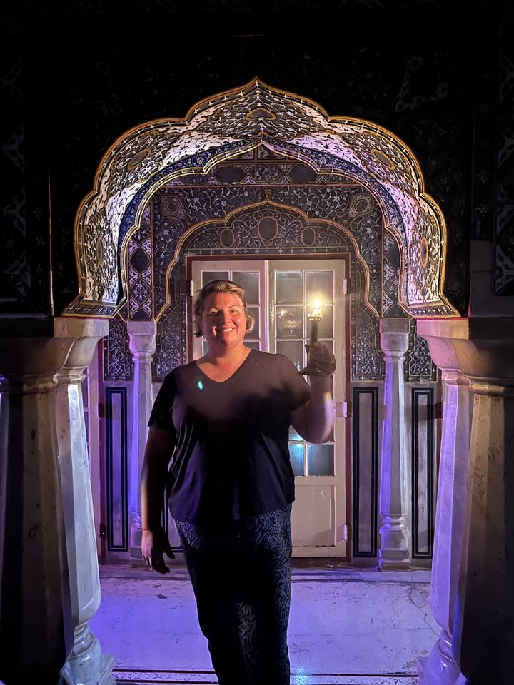 Individu tenant une bougie dans un intérieur richement décoré.