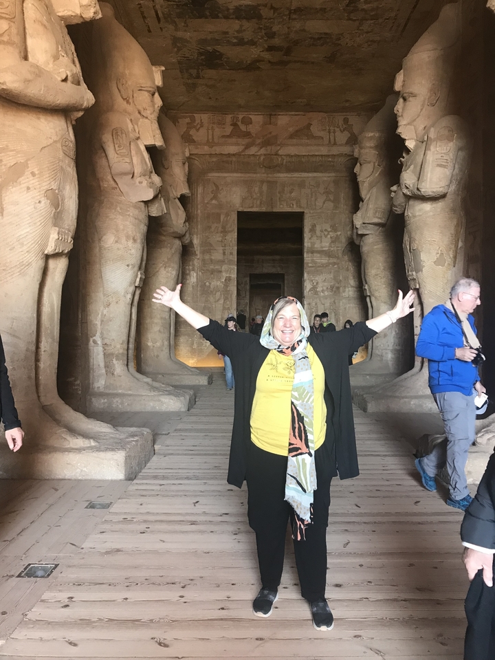 Une personne souriante debout à l'intérieur d'un temple égyptien antique avec de grandes statues.