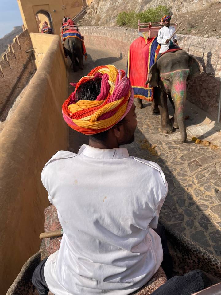 Persoon die een kleurrijke tulband draagt en op een olifant rijdt over een kasseienpad.