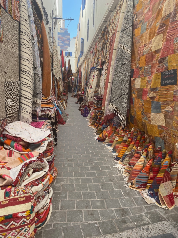 Ruelle de marché bordée de textiles et tapis colorés.