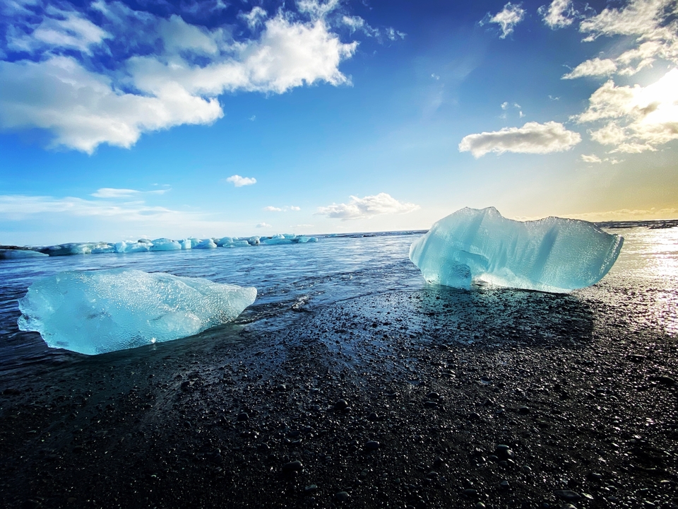 Icebergs on a black sand beach with a bright sky.