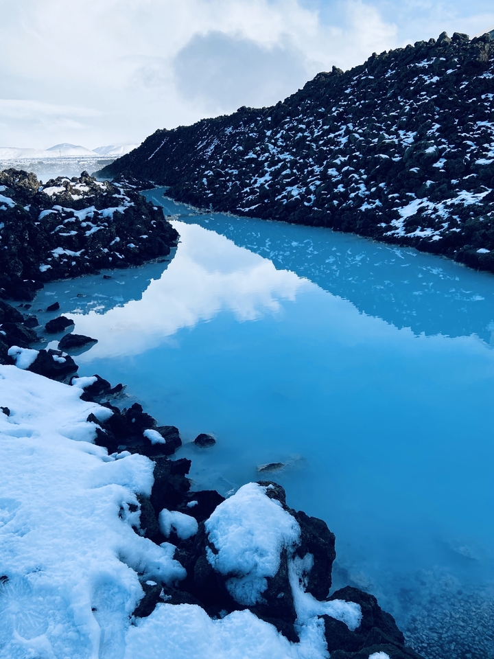 Bright blue geothermal pool surrounded by rocky terrain.