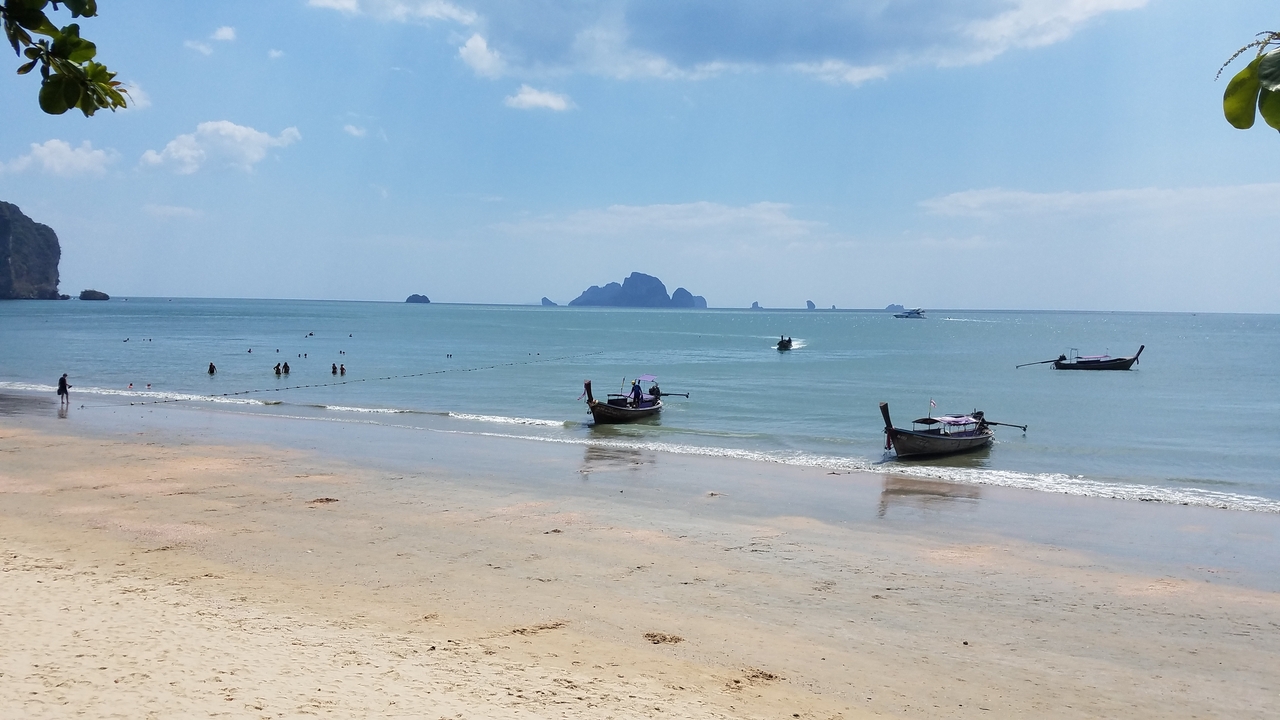 Beach with long-tail boats and swimmers in the ocean.