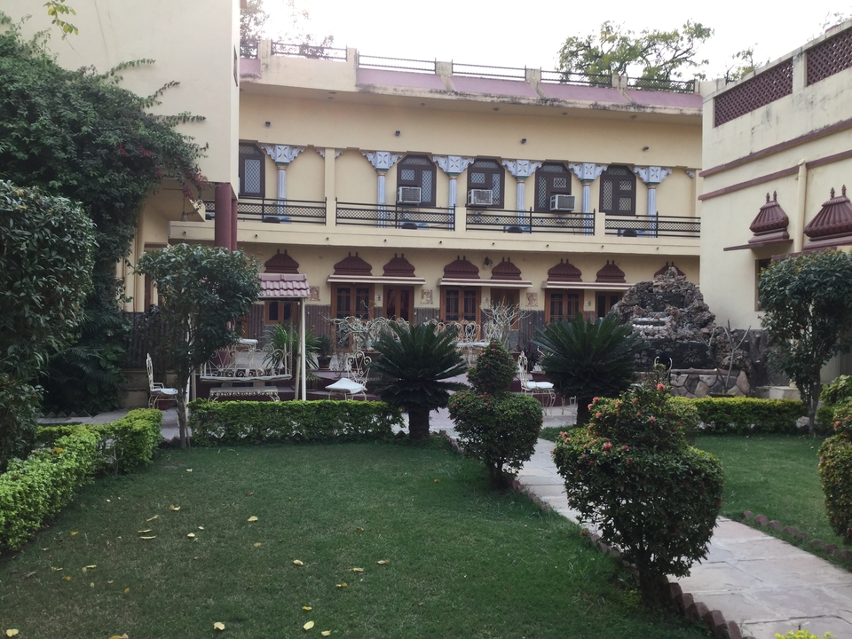 Traditional courtyard garden of Indian heritage hotel with manicured hedges, palms and yellow stucco façade.