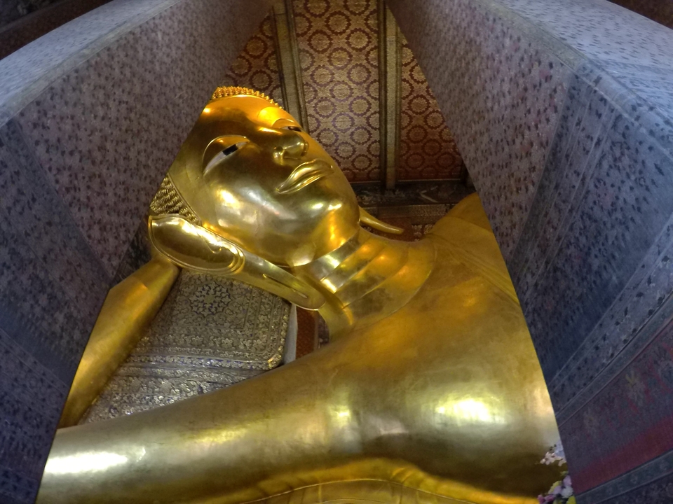 Statue dorée de Bouddha couché à l'intérieur d'un temple orné.