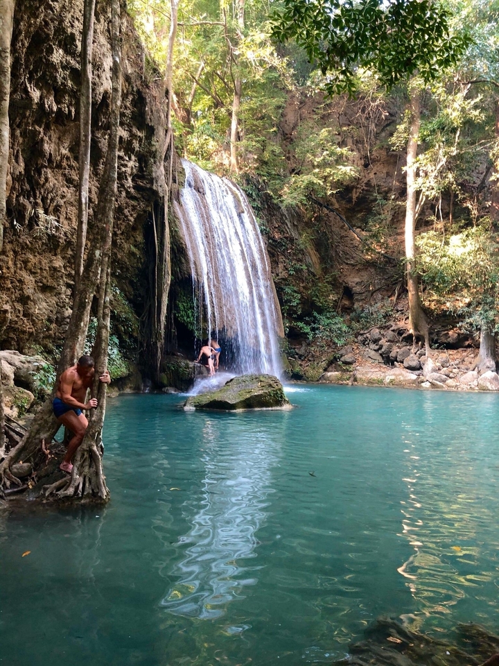 Cascade d'eau tombant dans un bassin turquoise avec des gens à proximité.