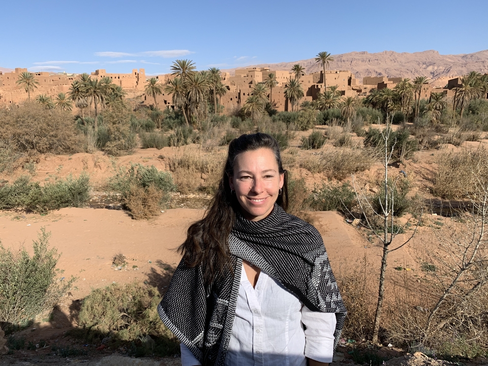 Femme souriante avec architecture désertique et palmiers en arrière-plan.