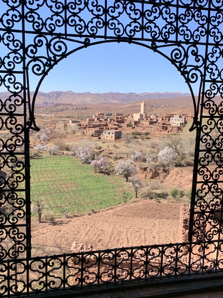 Vue d'un village marocain à travers une arche décorative avec des champs au premier plan.