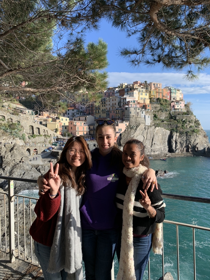 Three friends pose with the colorful cliff-side village of Manarola and the sea behind