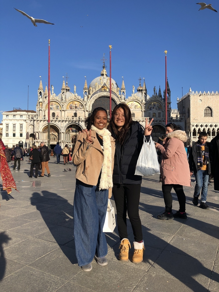 Two travelers flashing peace signs in front of St. Mark’s Basilica in Venice