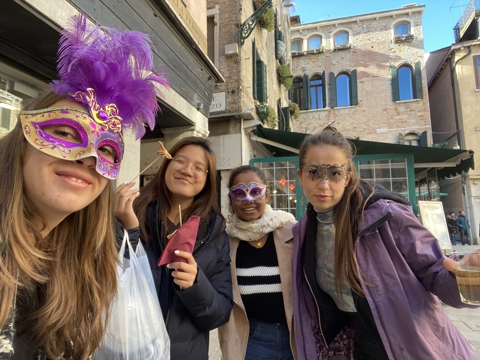 Group wearing colorful Venetian carnival masks pose in a lively street market
