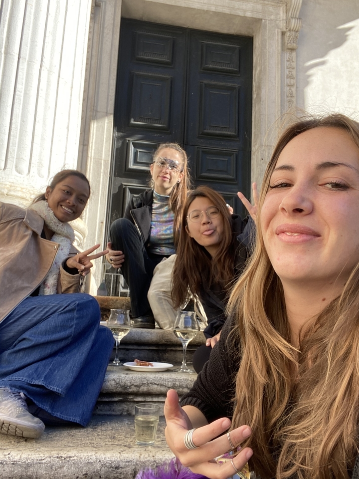 Four friends relax on marble steps, posing playfully for a selfie